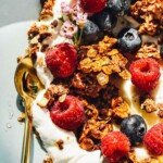 yogurt in a bowl with granola, rapsberries, blueberries, with a gold spoon.