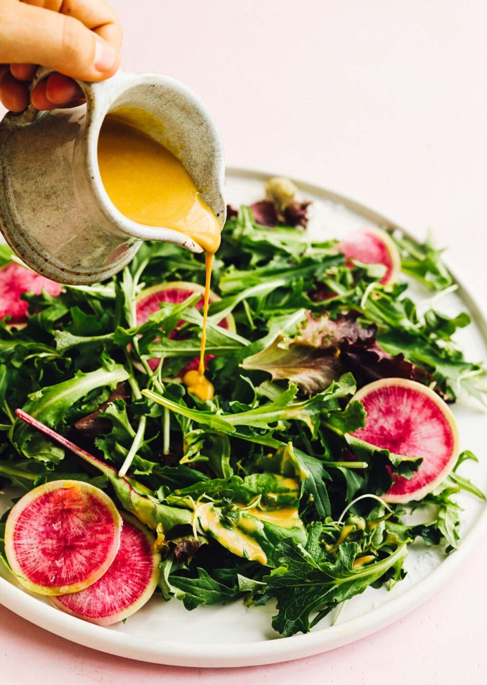 pouring creamy vegan salad dressing onto greens