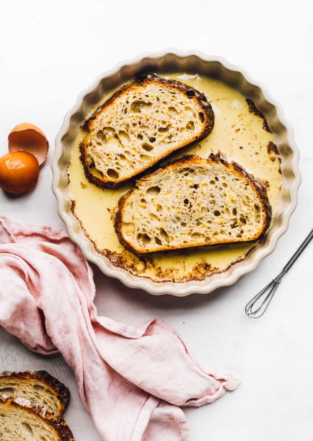 bread soaking in pan for french toast, whisk next to the dish and pink linen.