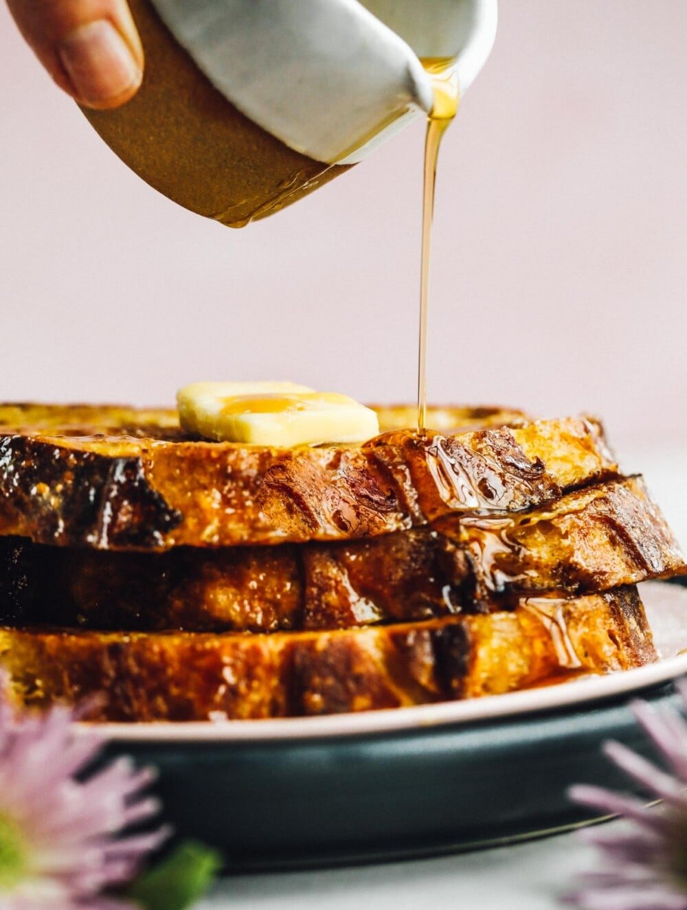 pouring maple syrup on stacked slices of sourdough french toast