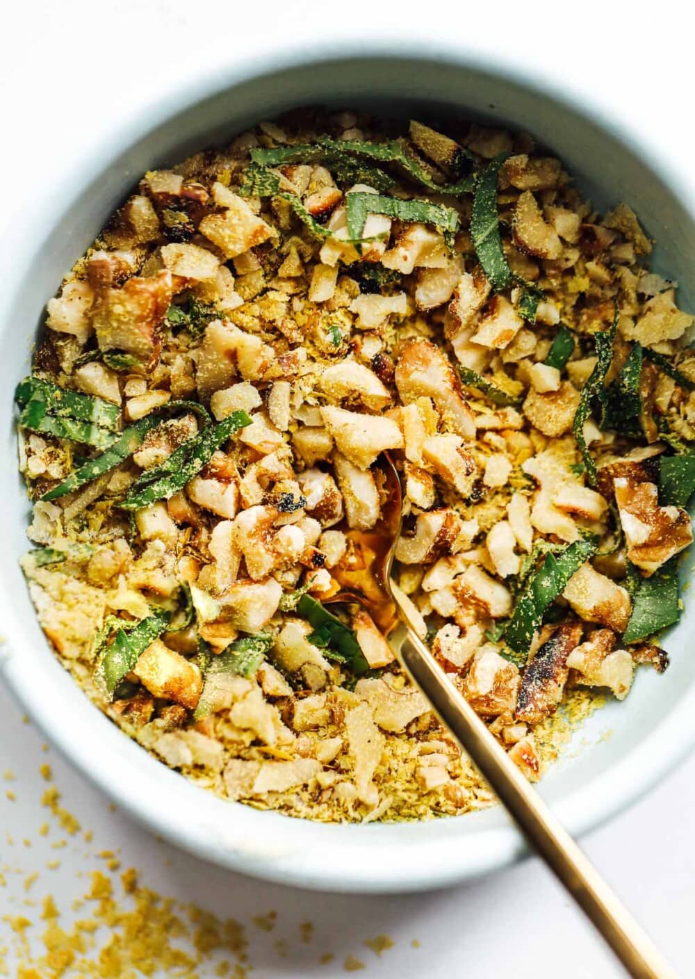 nutritional yeast crunch in a blue bowl with gold spoon