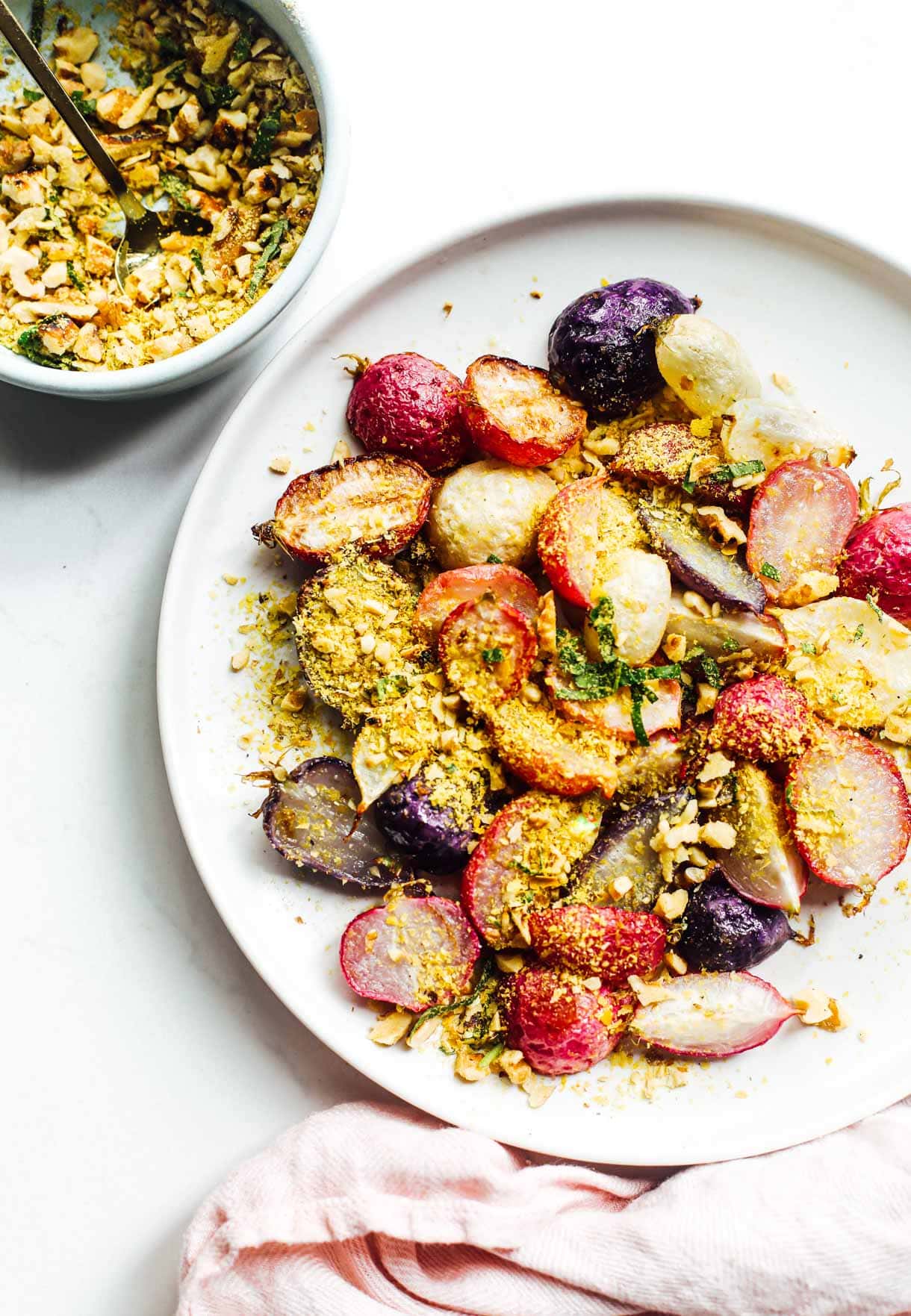 roasted radishes on a white plate with walnut nutritional yeast topping