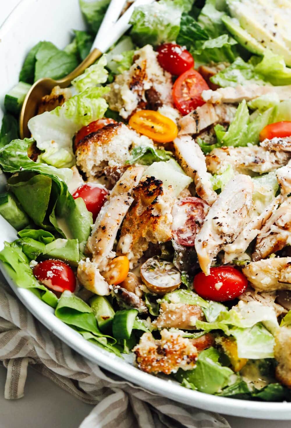 grilled chicken caesar salad in bowl with gold utensils