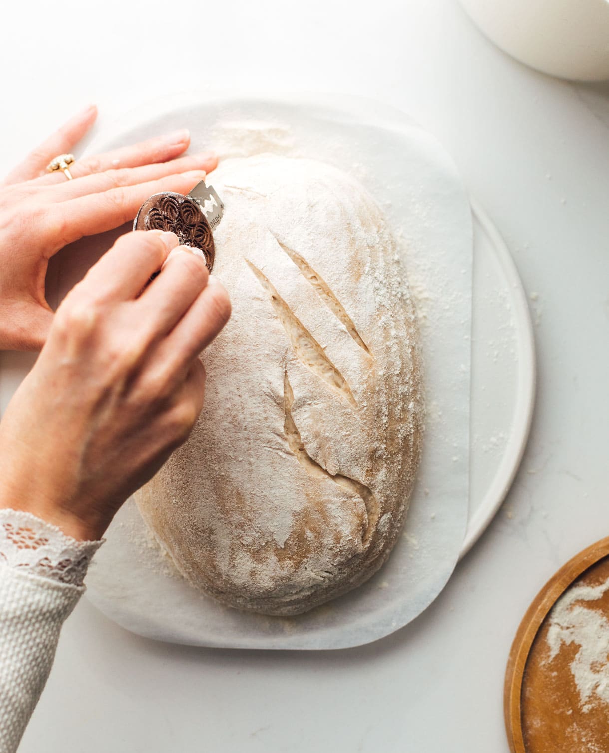woman scoring sourdough bread with bread lame 