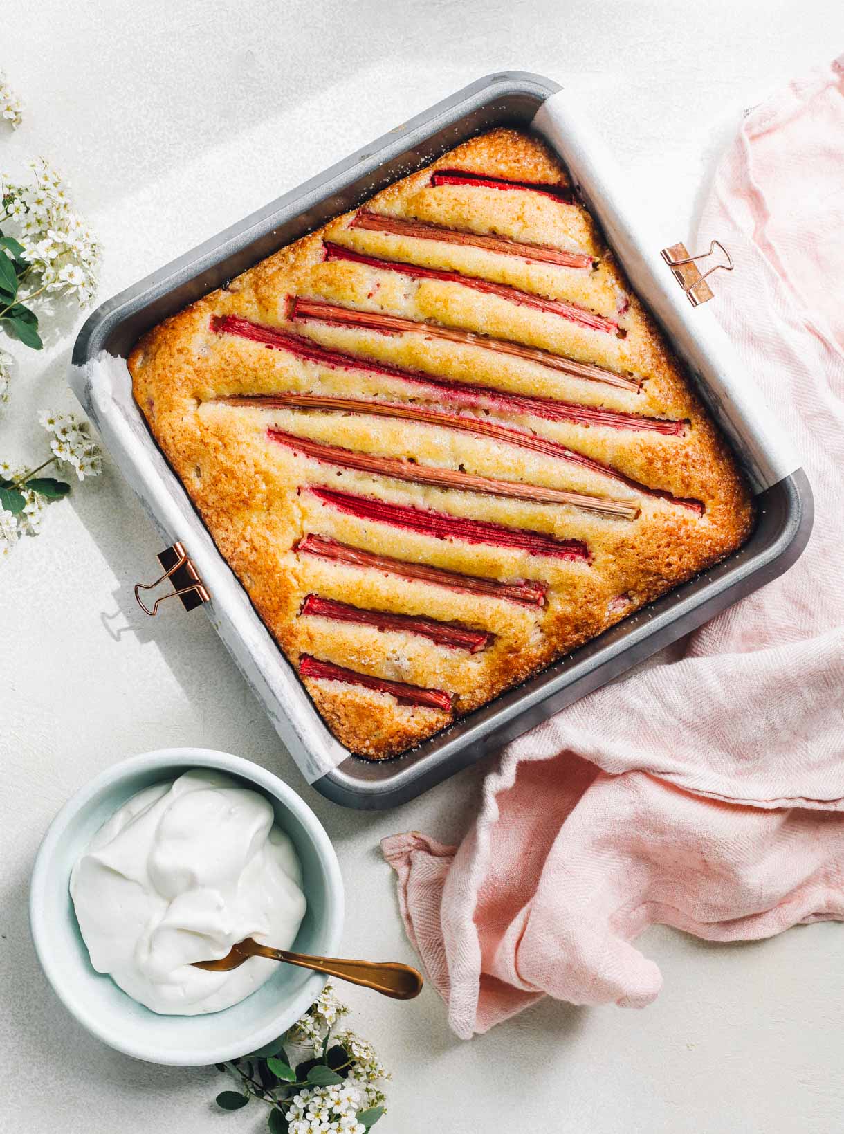 sourdough discard rhubarb cake in a square pan with bowl of whipped cream to the left.