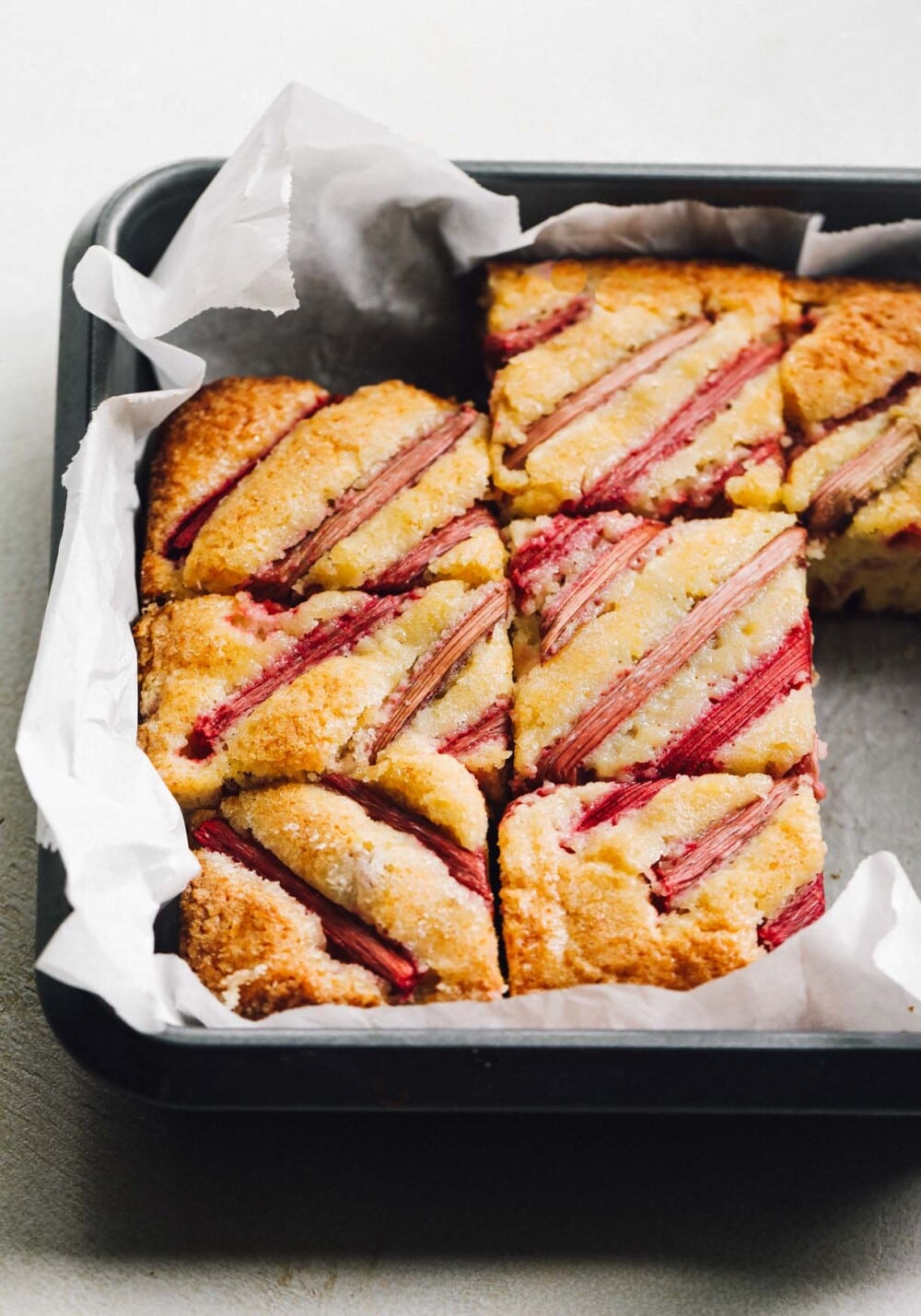 sourdough rhubarb cake cut into pieces in a baking pan