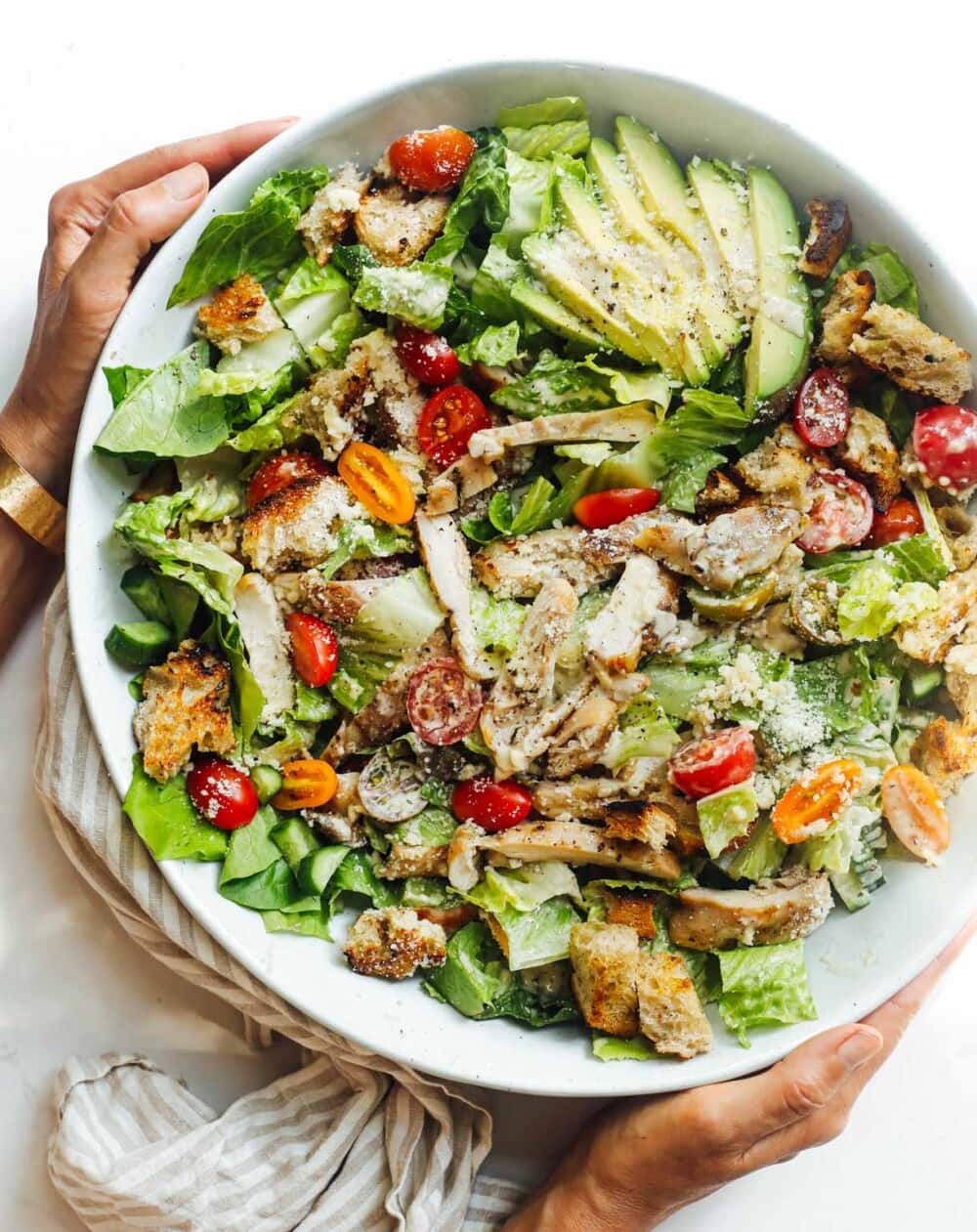 grilled chicken caesar salad in a large bowl, with woman holding it