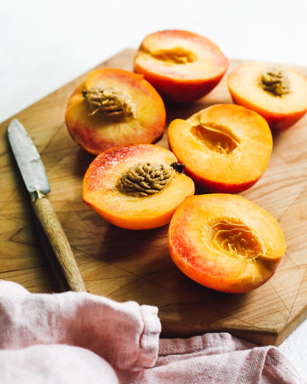 peaches sliced in half on a wooden cutting board