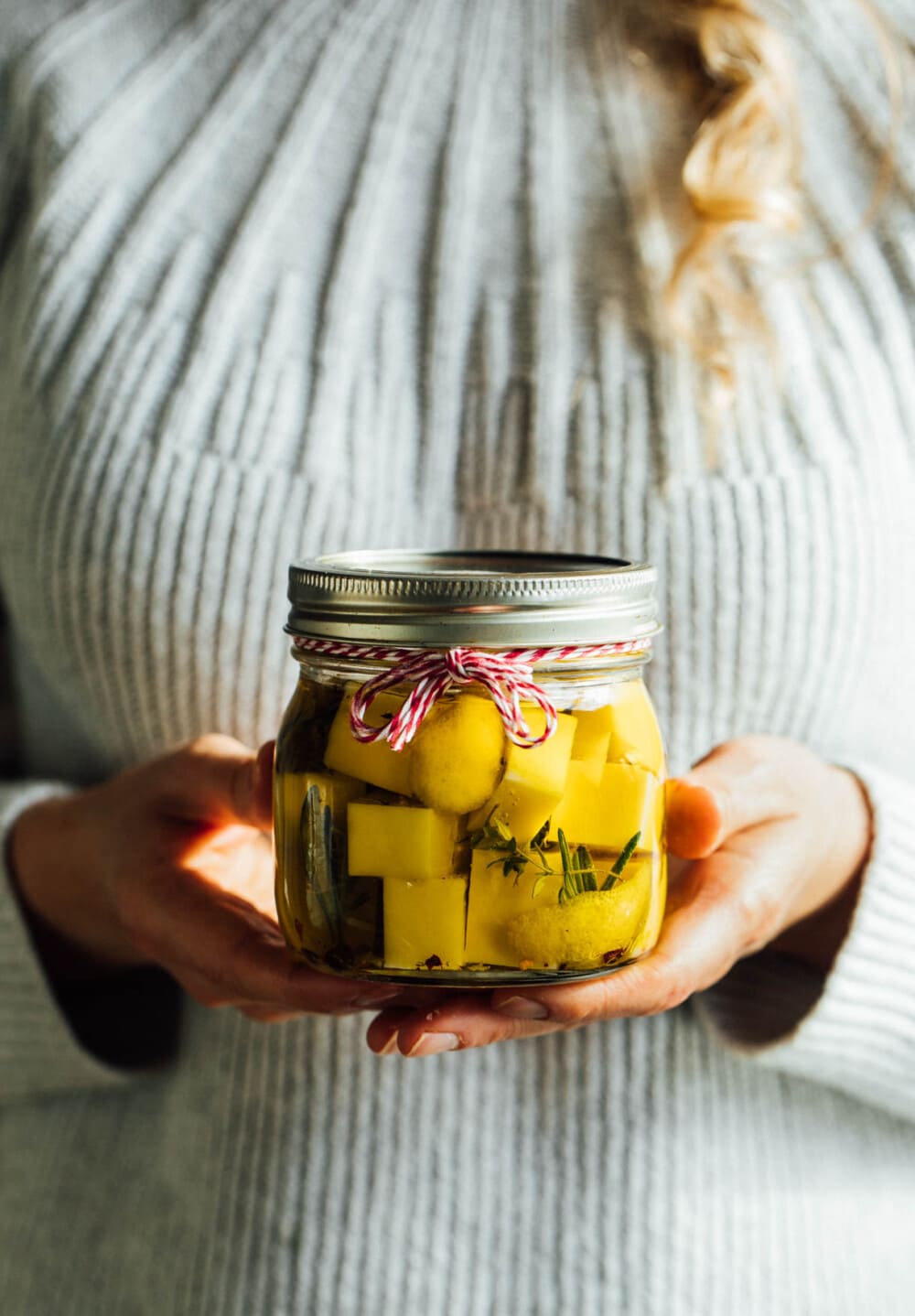 woman holding marinated cheese in ball jar.