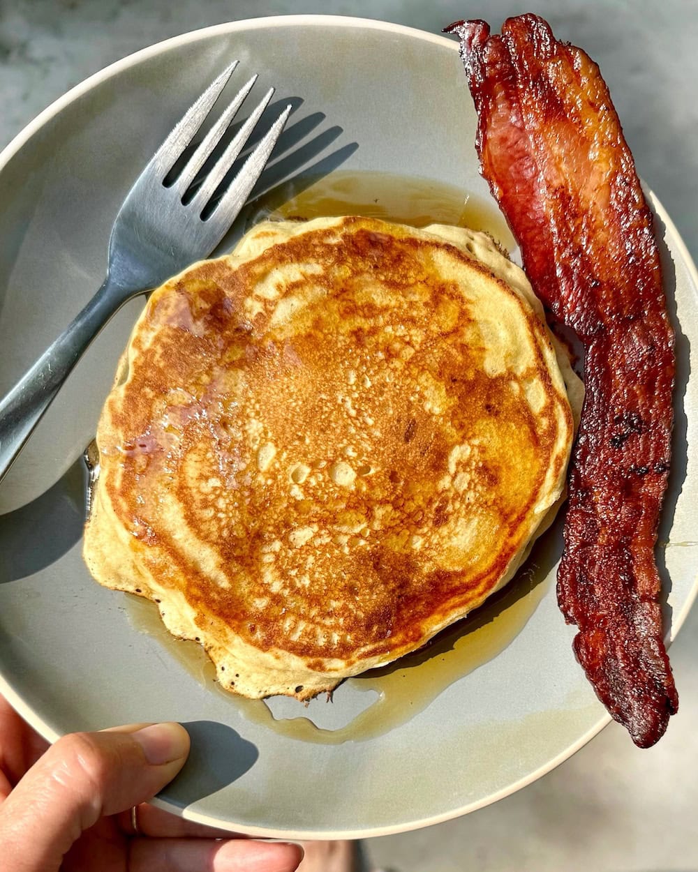 sourdough pancake and bacon on a grey plate with fork to the left.