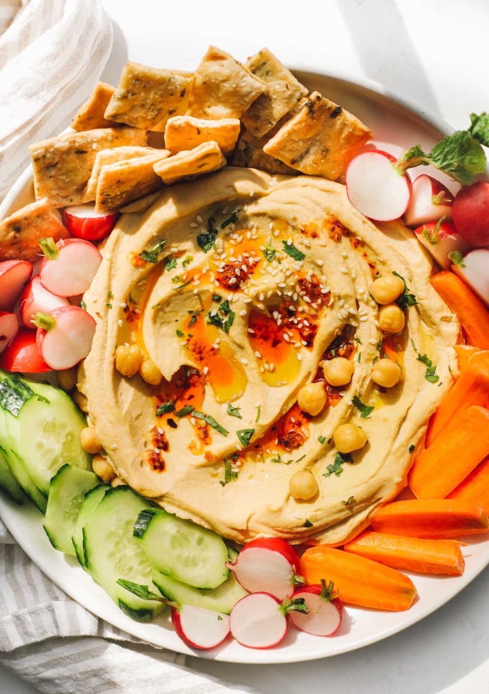 hummus on white plate surrounded by fresh vegetables and crackers