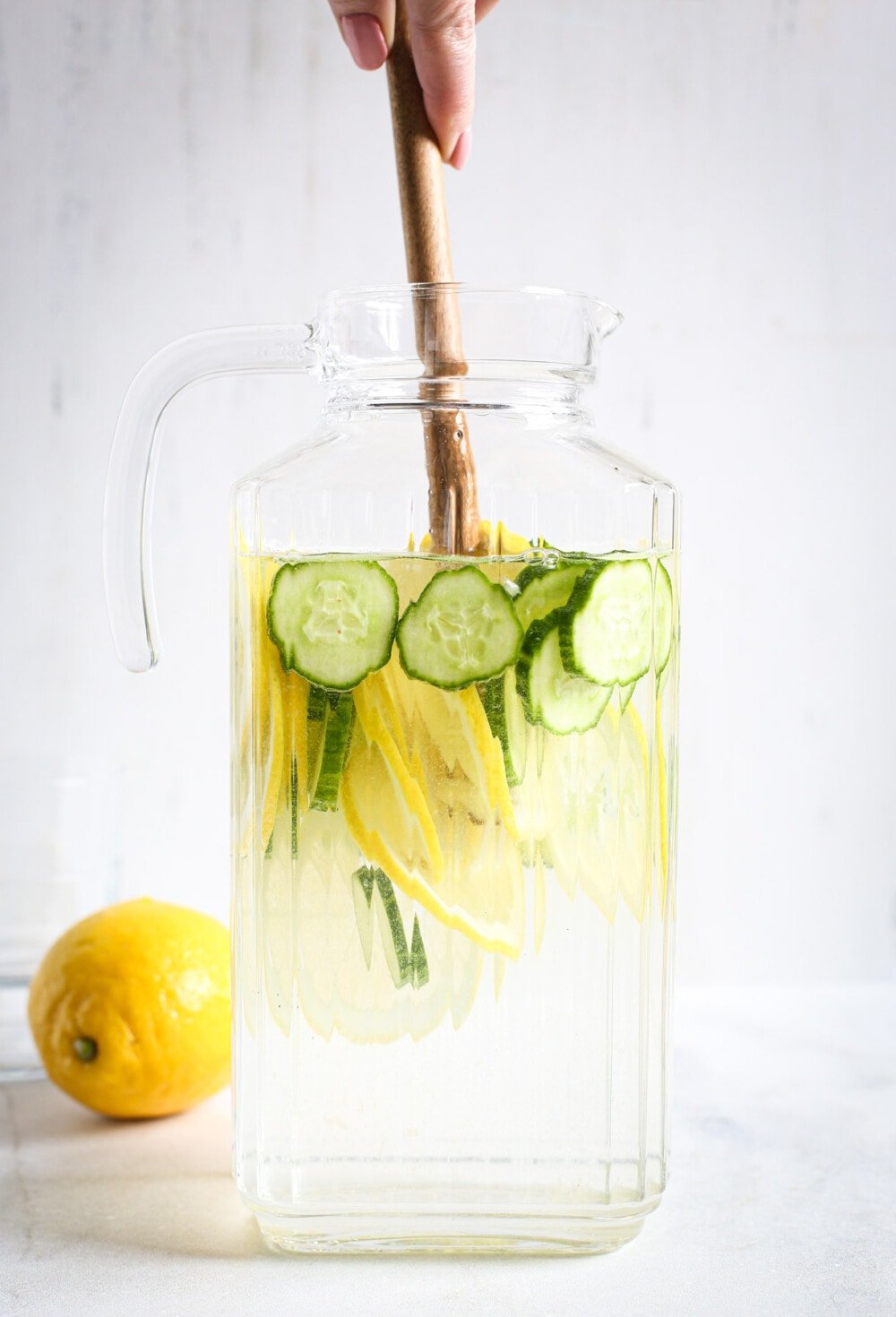 cucumber lemon water in a glass pitcher with someone stirring it