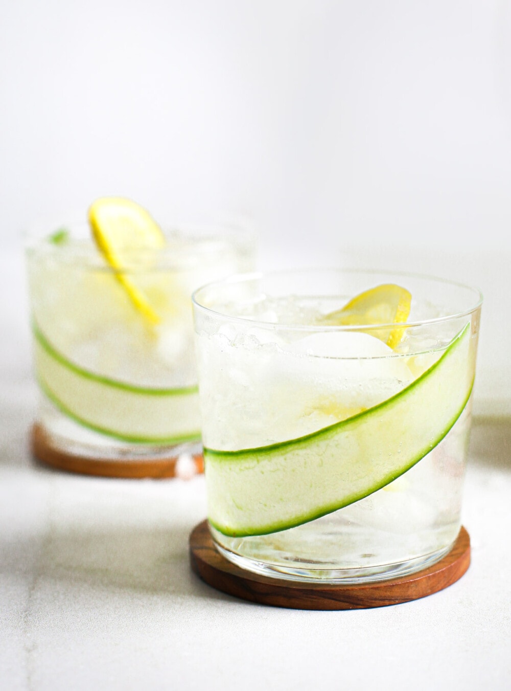 cucumber lemon water in clear glass, sitting on wooden coaster