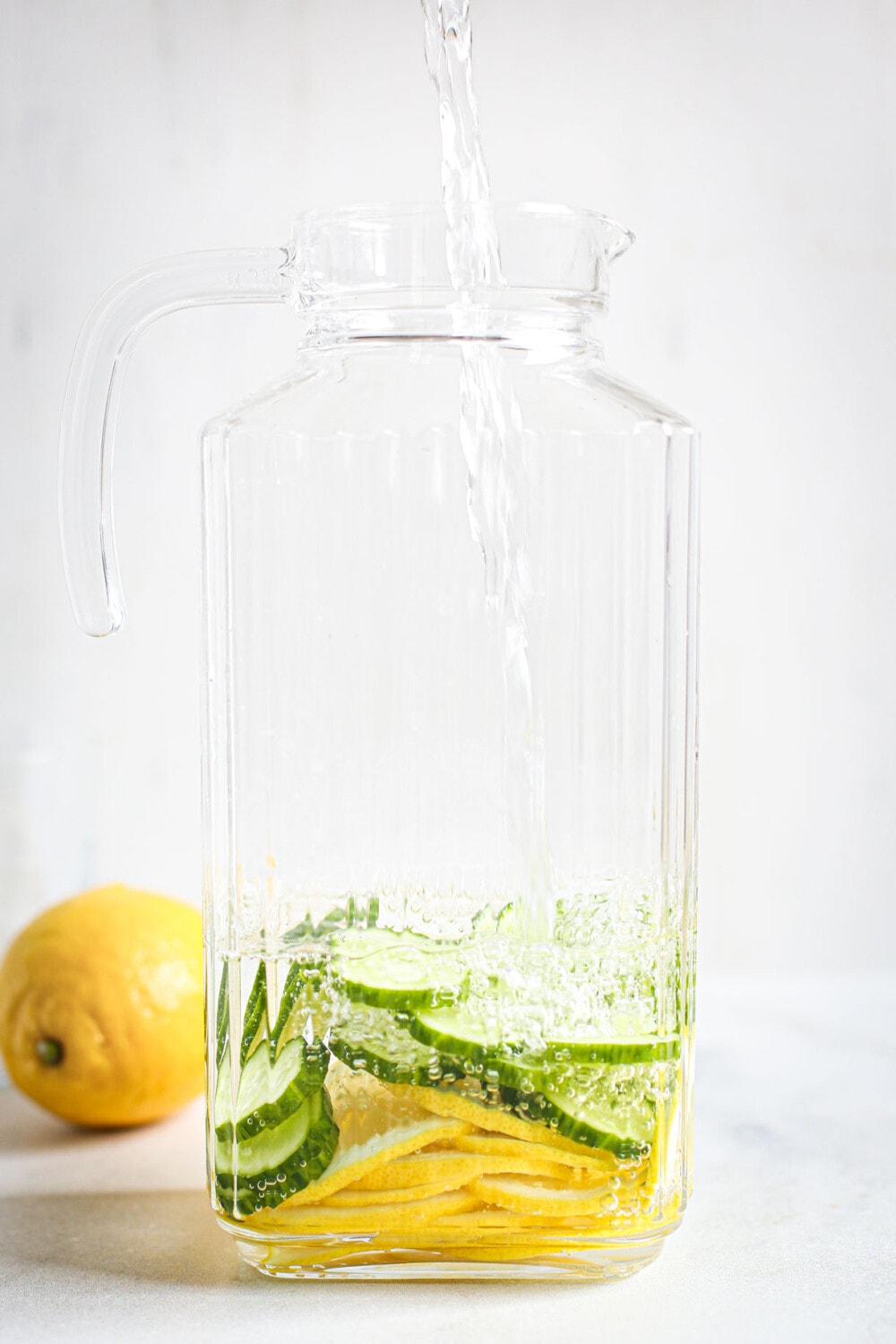 pouring water into glass pitcher filled with cucumbers and lemon slices