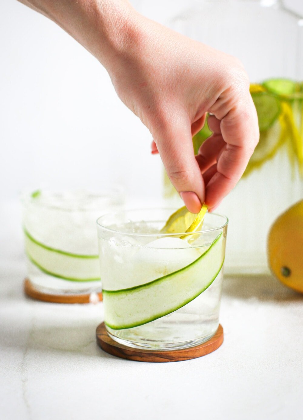 place lemon slice in a glass of cucumber water, clear glass.