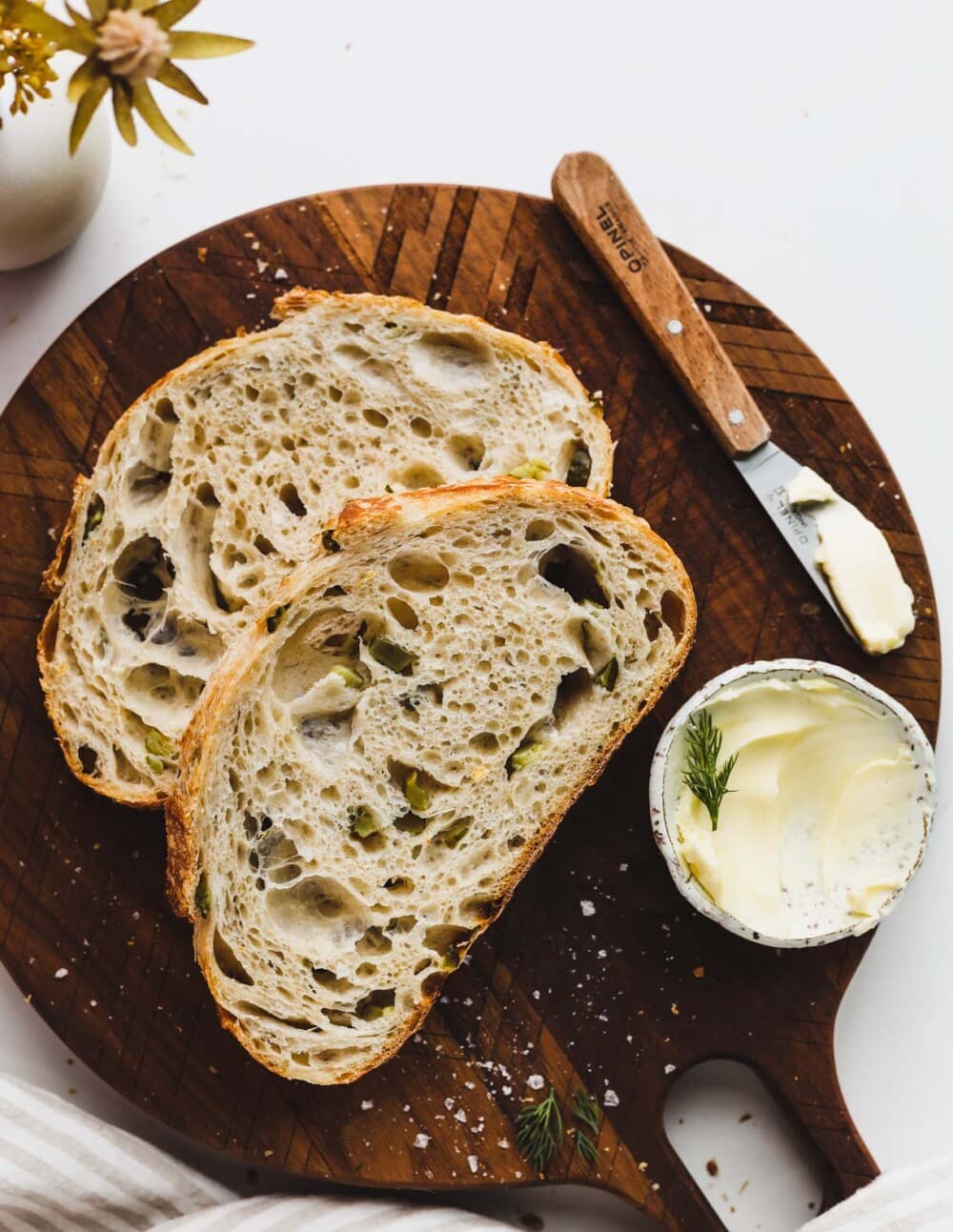 sliced dill pickle sourdough bread on cutting board with small bowl of butter and knife