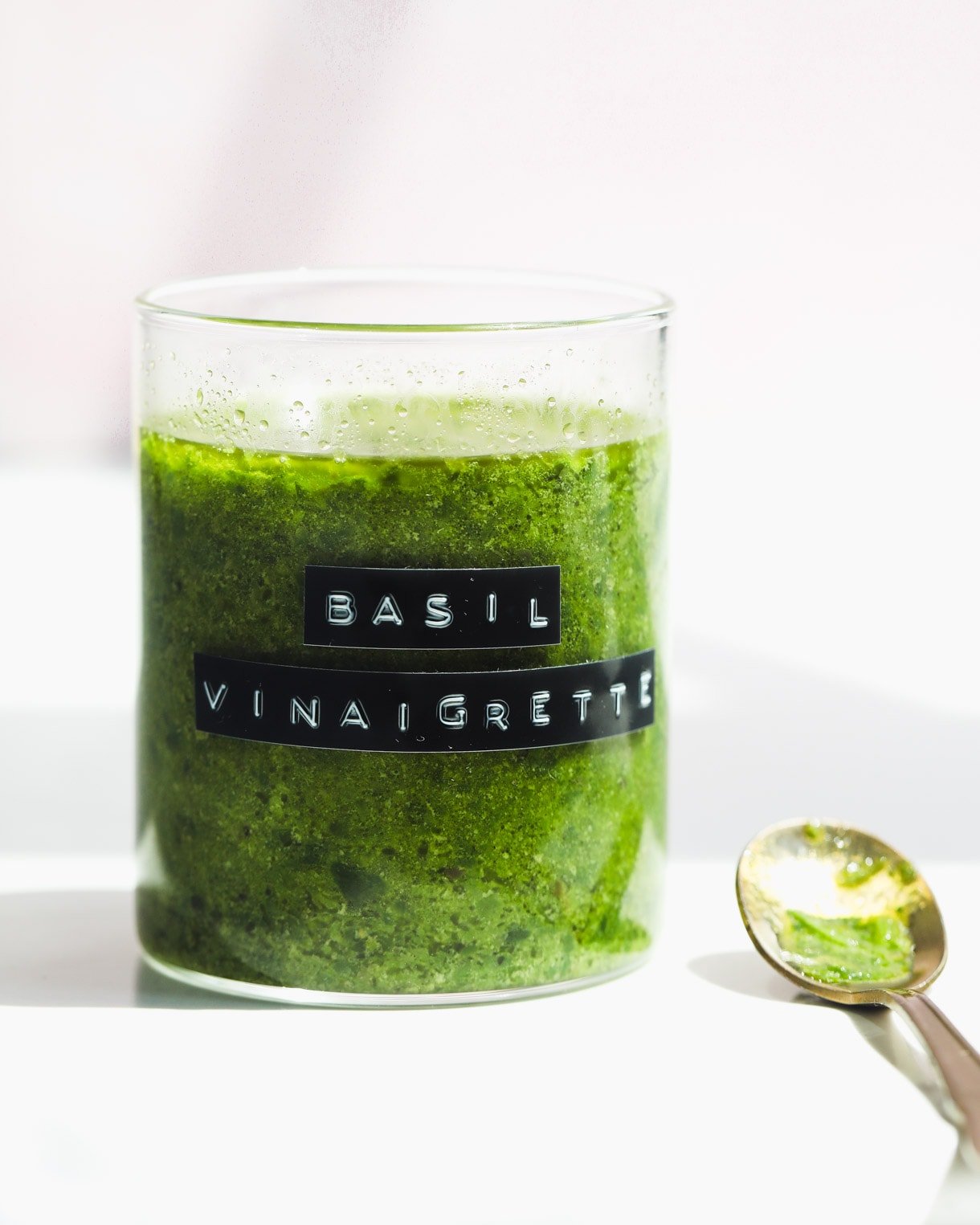basil vinaigrette in a glass jar with gold spoon next to it