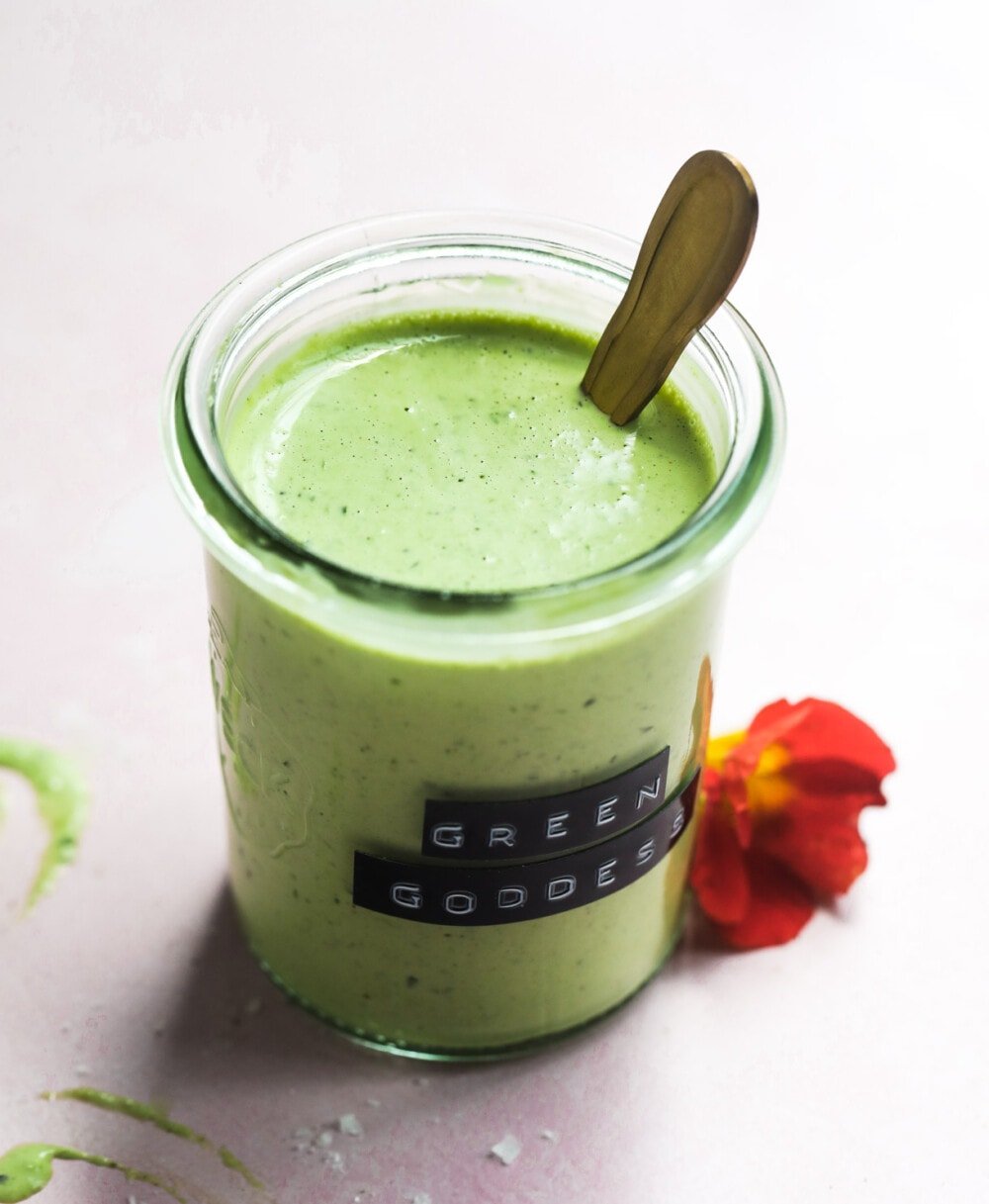 green goddess dressing in a small clear jar with red flower next to it
