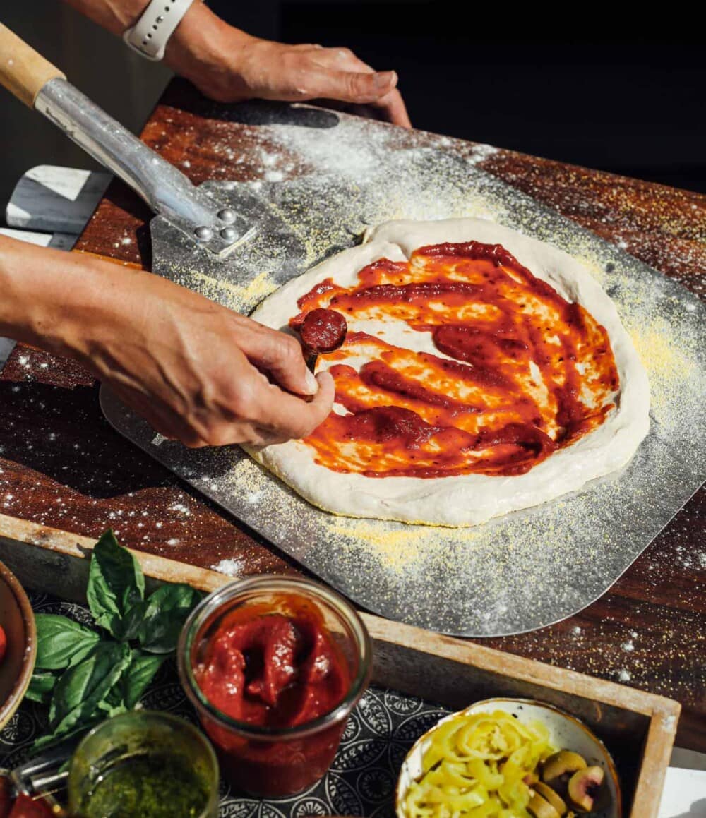 putting pizza sauce onto pizza dough that is sitting on a pizza peel