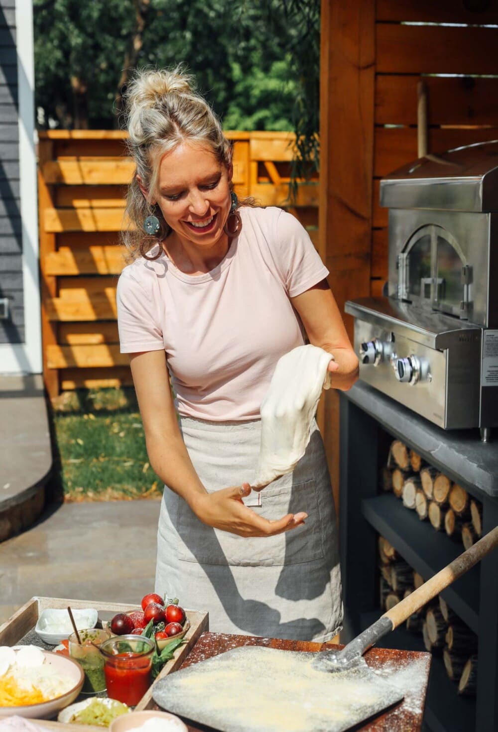 blonde woman tossing pizza dough outside
