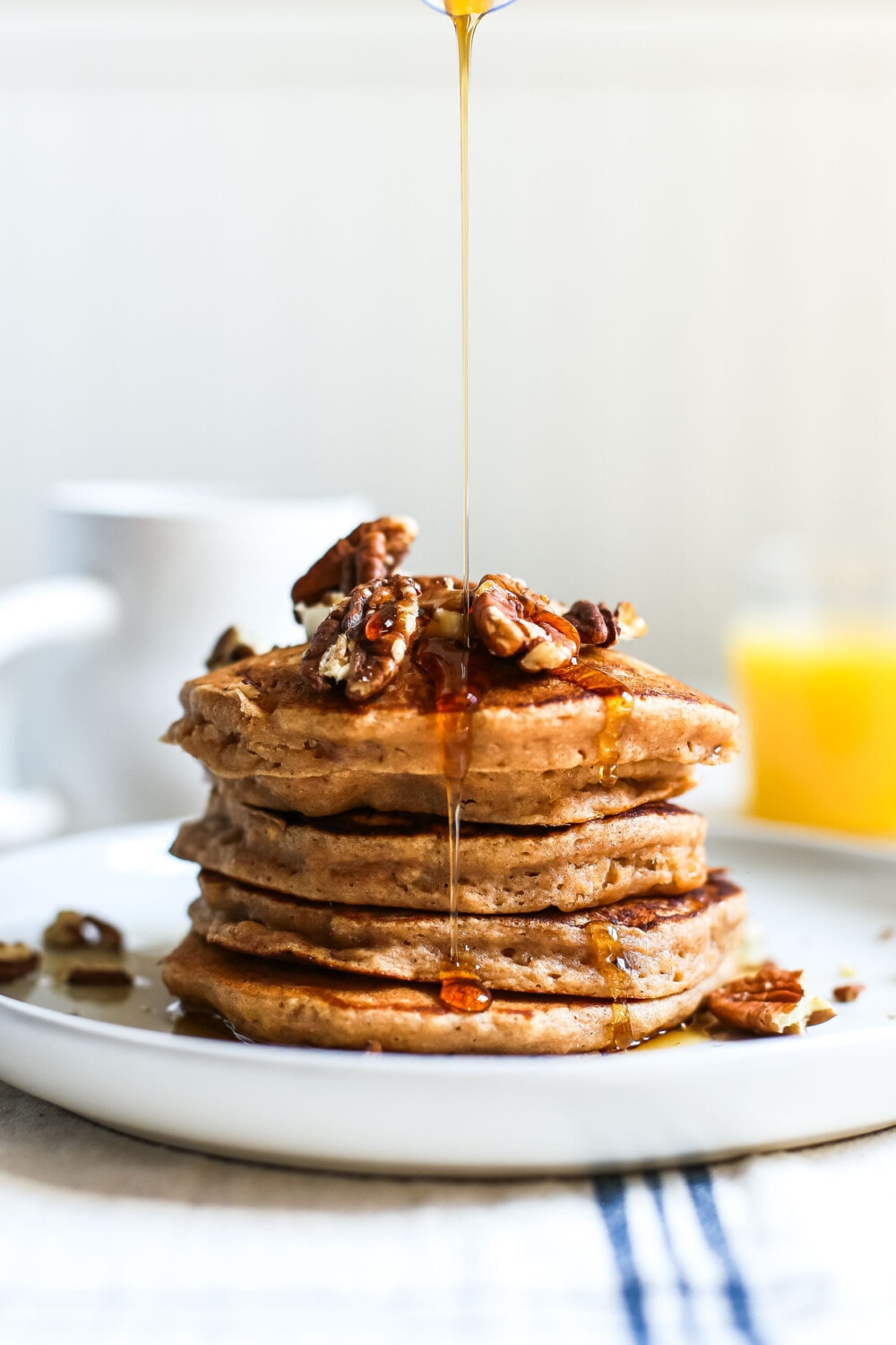apple butter pancakes stacked on a white plate with maple syrup drizzling over the top