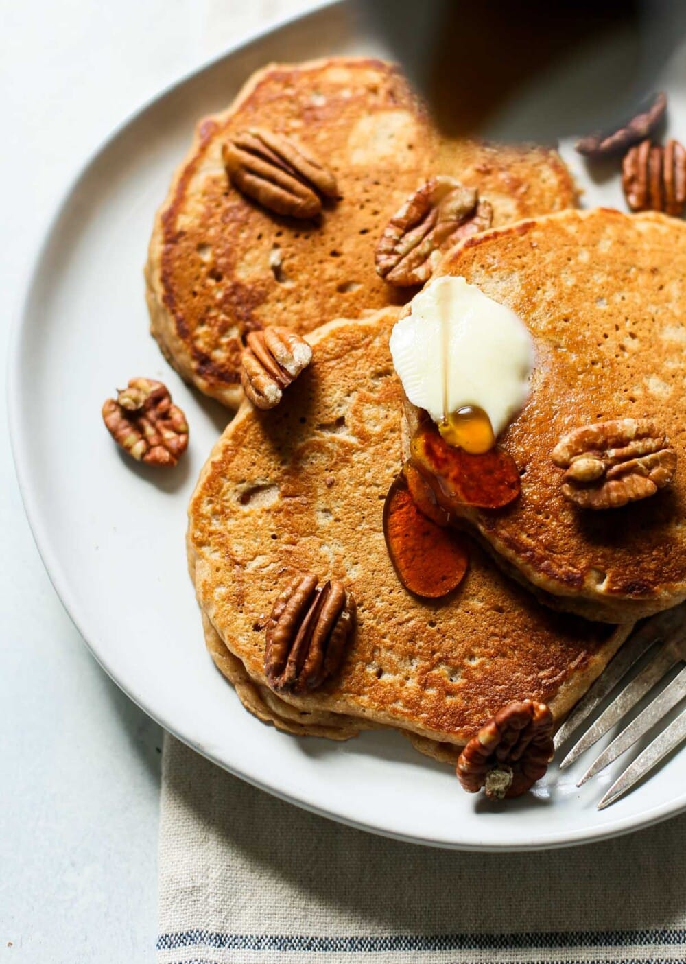 apple butter pancakes on a plate with maple syrup drizzle and butter, pecans