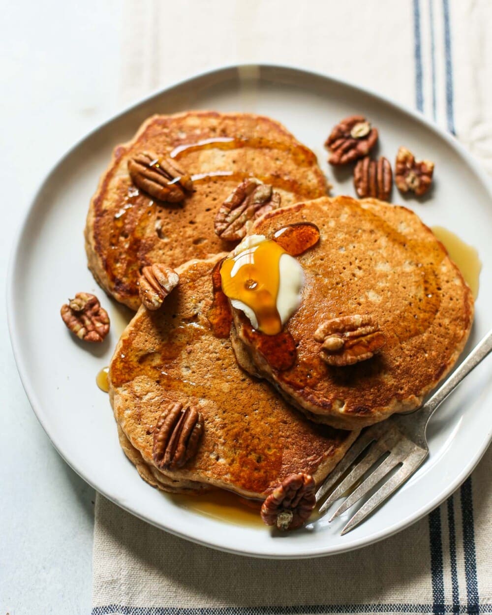 apple butter pancakes with maple syrup and pecans on a white plate