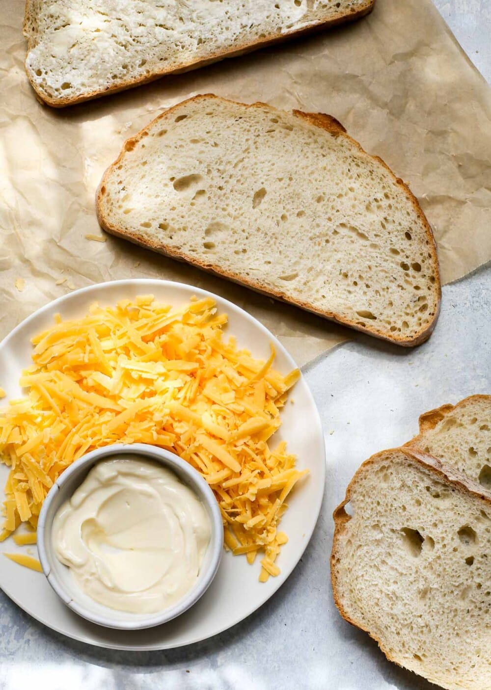 white bread on parchment with grated cheese next to it on a plate