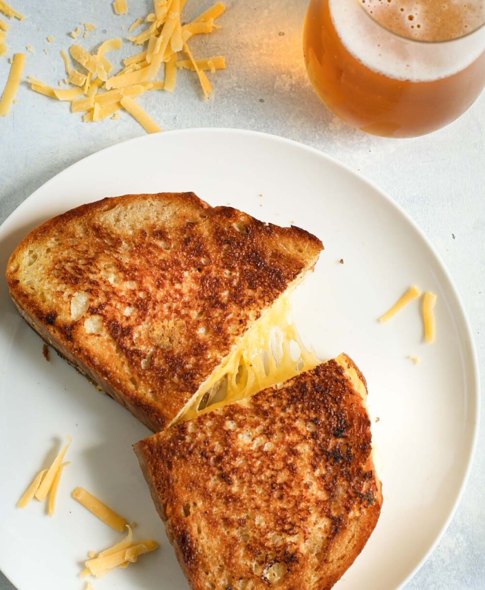 sourough grilled cheese on a white plate, cut in half and cheese stretched