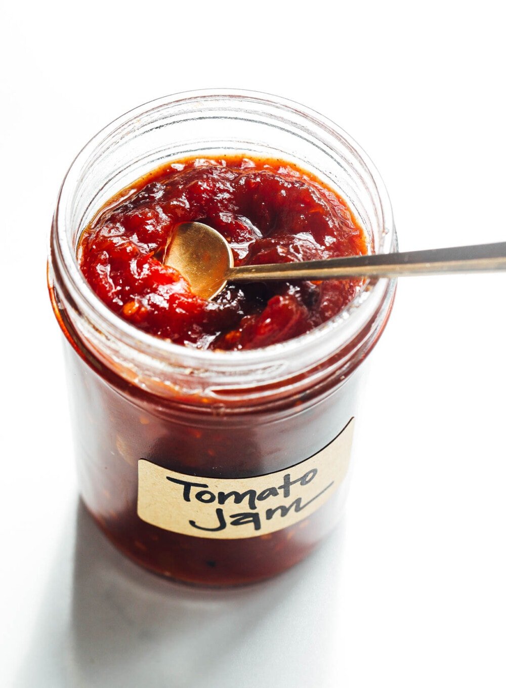 tomato jam in a clear jar with gold spoon