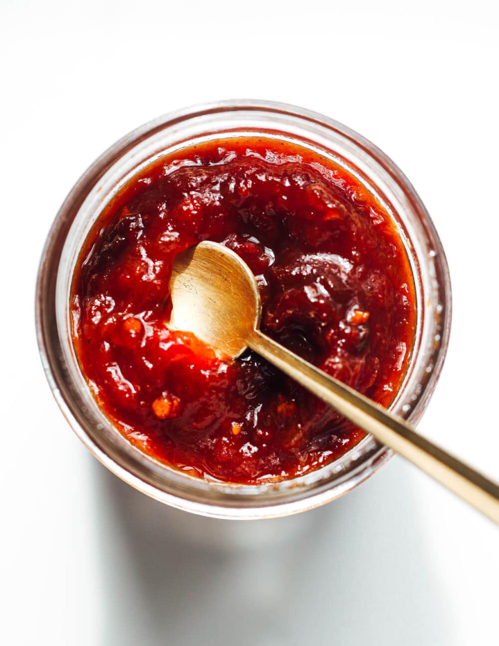 tomato jam in a clear jam with a gold spoon in it
