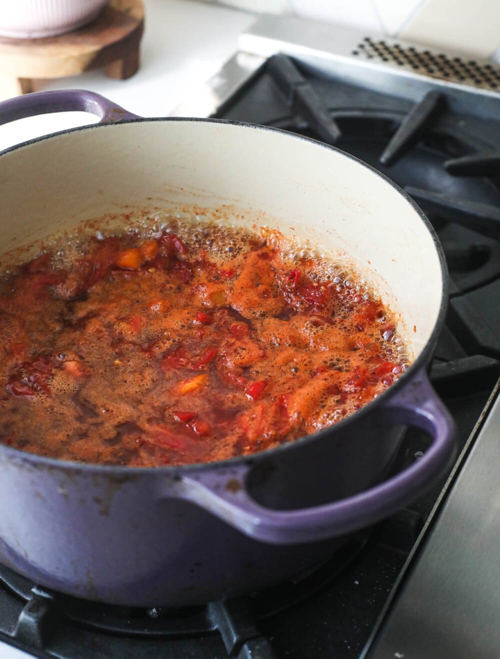tomato jam simmering on the stove in a purple handled pot