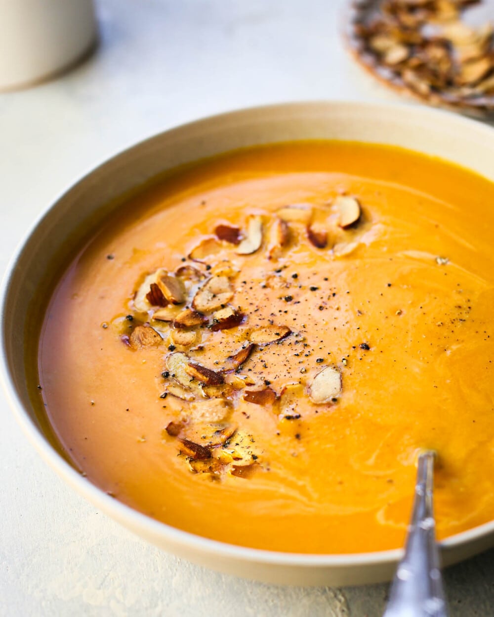 butternut squash bisque in white bowl with almonds on top