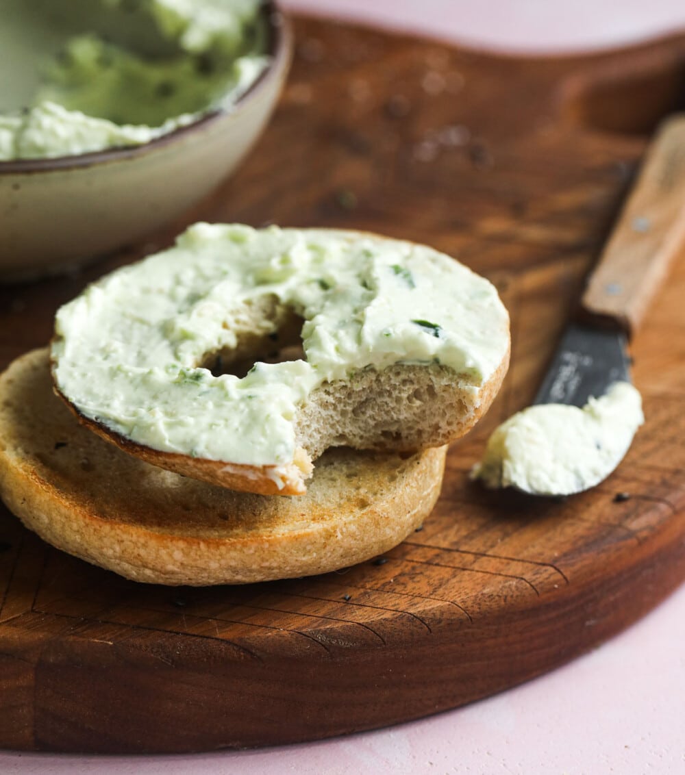 jalapeno cream cheese on a bagel with knife next to it, on wooden cutting board