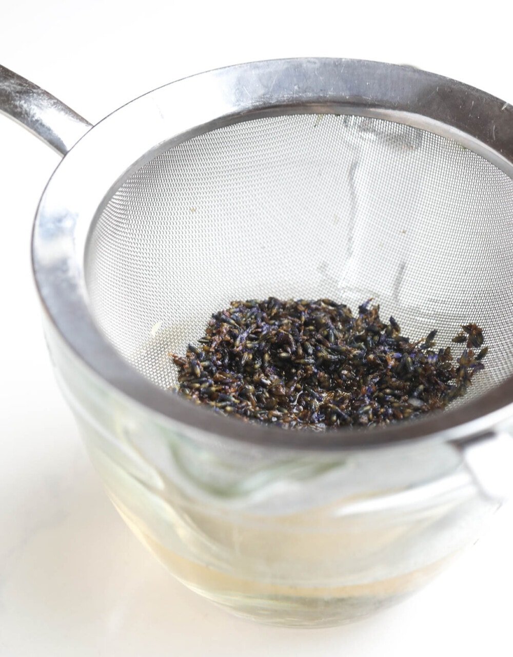 straining lavender buds into a glass bowl