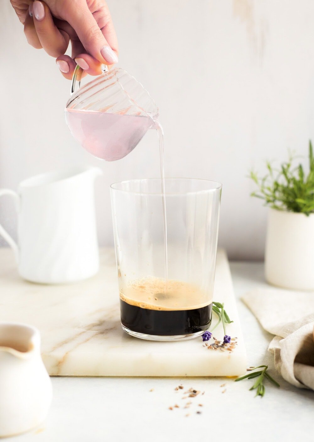 pouring lavender syrup into a clear glass with espresso