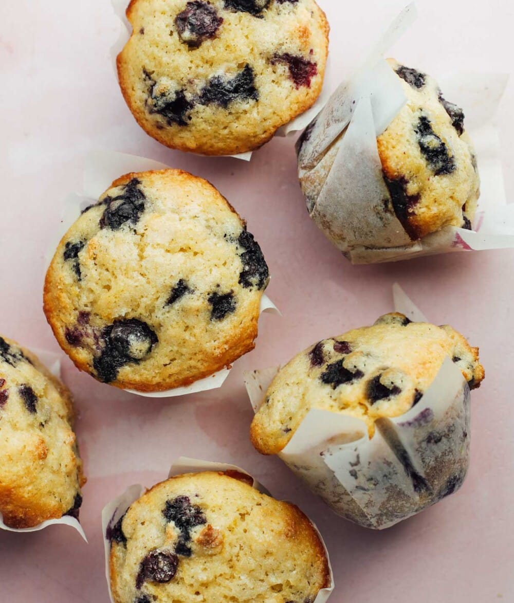 blueberry muffins in white liners on a pink backround