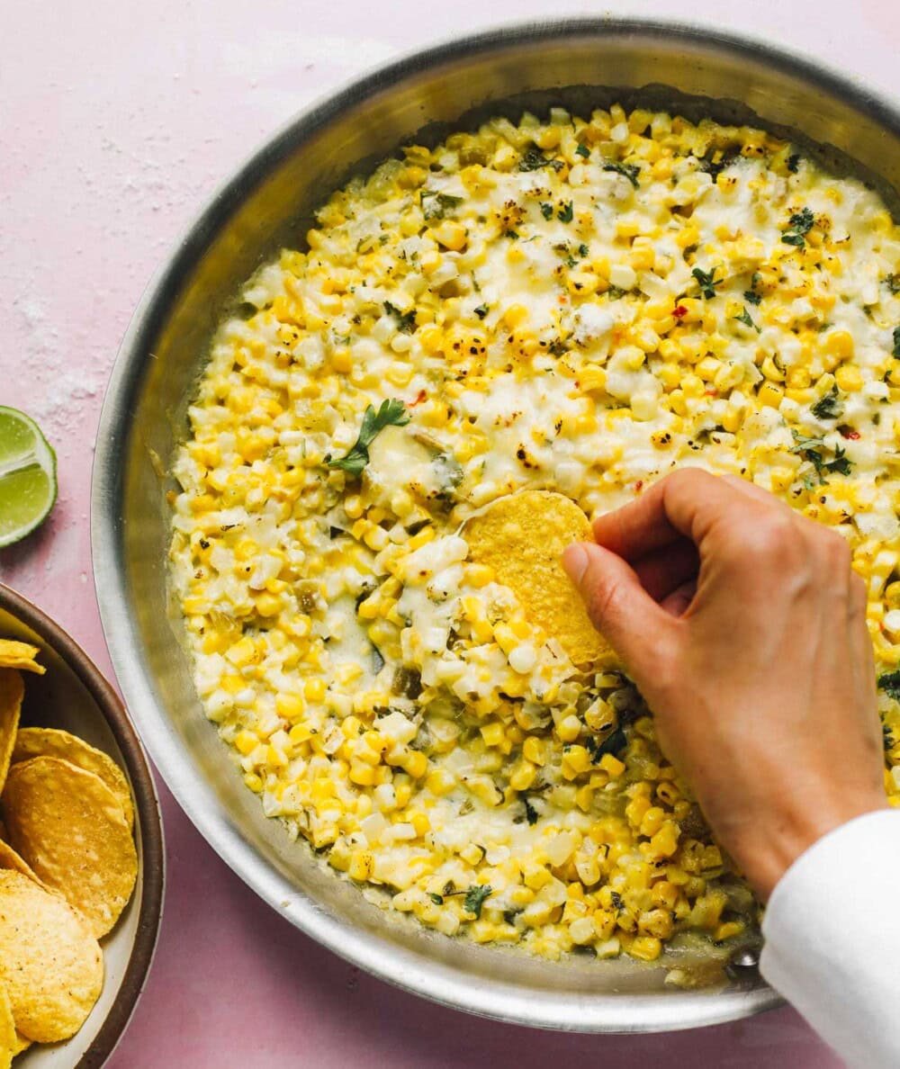 Corn dip with tortilla chips and hand dipping with a chip
