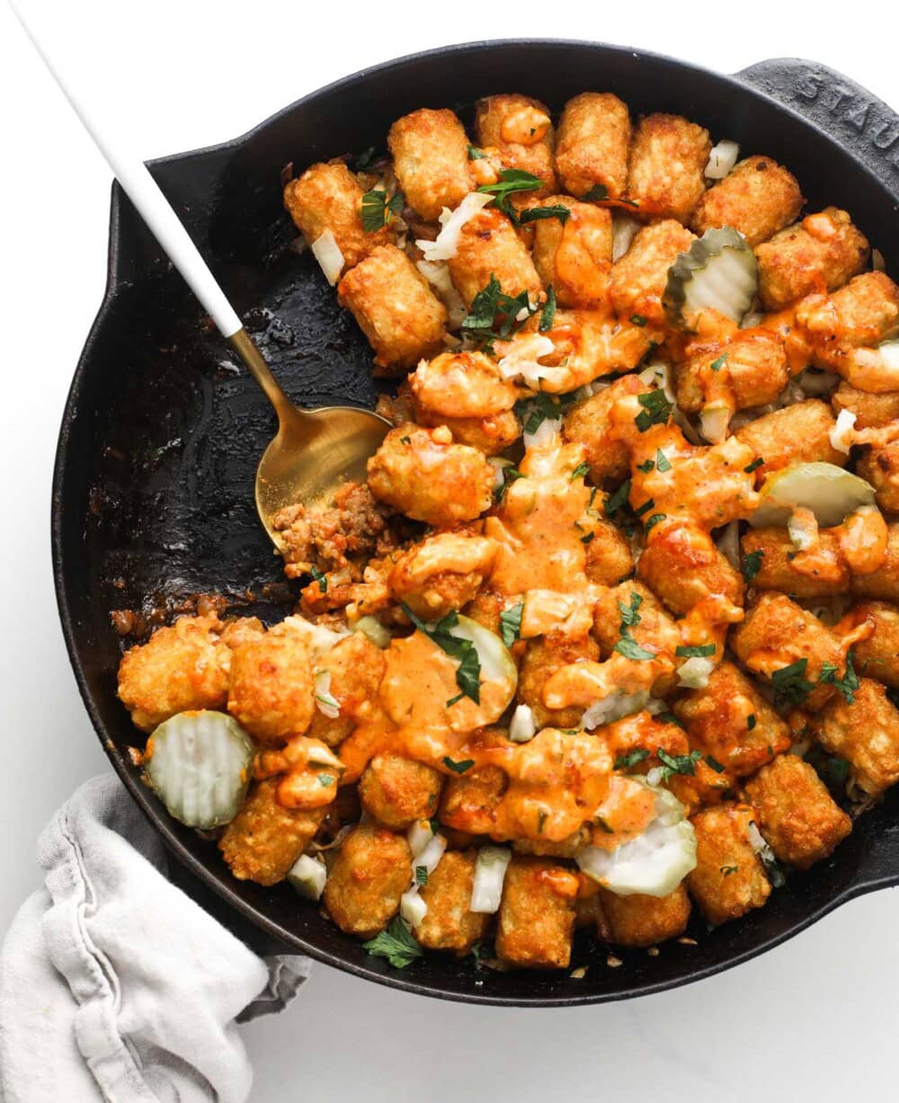 cheeseburger tater tot hotdish baked in black cast iron skillet with gold spoon