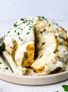 whole roasted cauliflower on a plate with cheese sauce