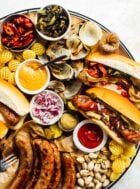 grilled brats on a party tray with condiments like ketchup, mustard, onions