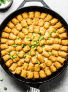 tater tot hotdish baked in a cast iron skillet with green onion garnish.