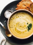 Bowl with green tomato soup on blue plate, with bowl of salt and sourdough bread.